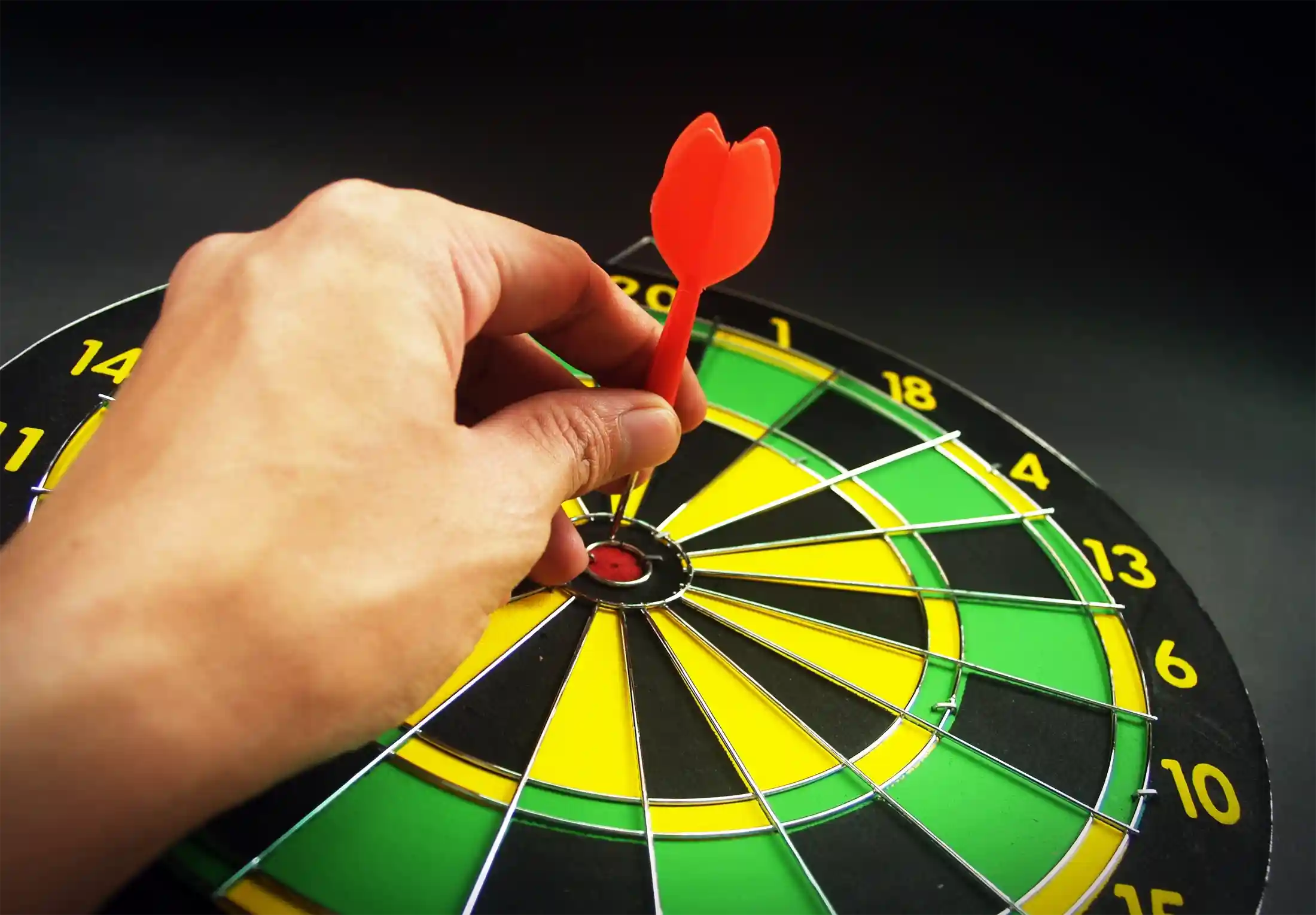 Person pulling a dart out of a bullseye on dart board
